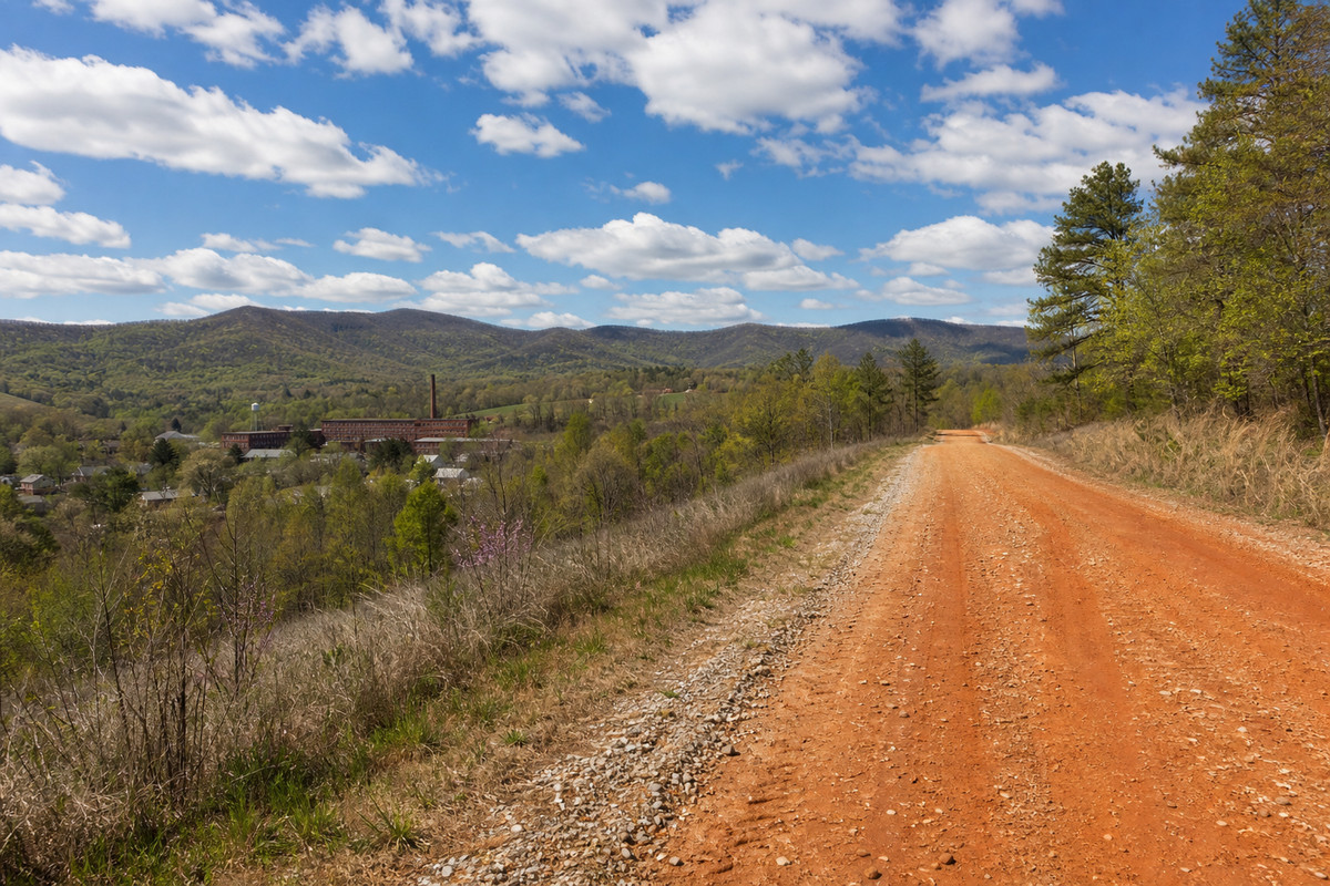 Red clay county road climbing into the South Carolina foothills above a mill town in early spring
